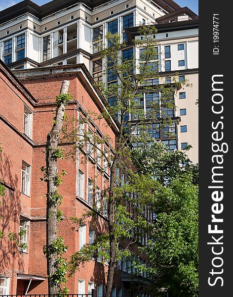 An old red brick house on the background of a tall contemporary apartment building. An old red brick house on the background of a tall contemporary apartment building