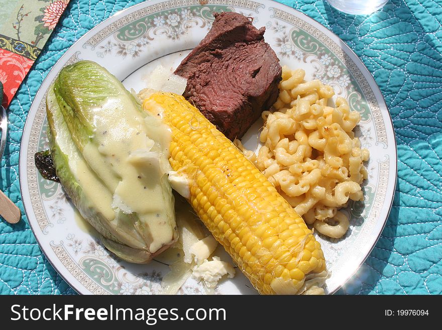 Plate of food with beef, corn, grilled romaine and macaroni and cheese. Plate of food with beef, corn, grilled romaine and macaroni and cheese.