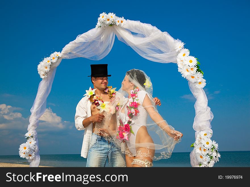 Groom with bride wearing lei, standing under archway on beach. Groom with bride wearing lei, standing under archway on beach