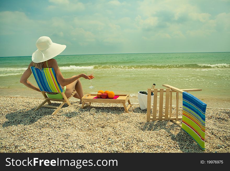 Lady in white hat sitting in chaise longue with glass of champagne. Lady in white hat sitting in chaise longue with glass of champagne