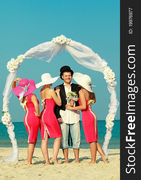Groom standing with bridesmaids under archway on beach. Groom standing with bridesmaids under archway on beach