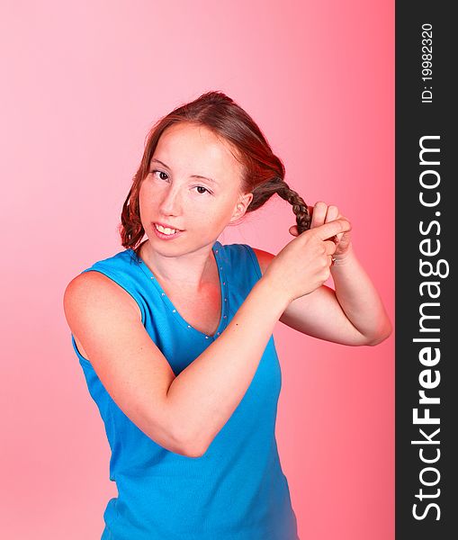 Sweet athletic girl in sporty blue t-shirt is making a hair braids on a red background. Sweet athletic girl in sporty blue t-shirt is making a hair braids on a red background.
