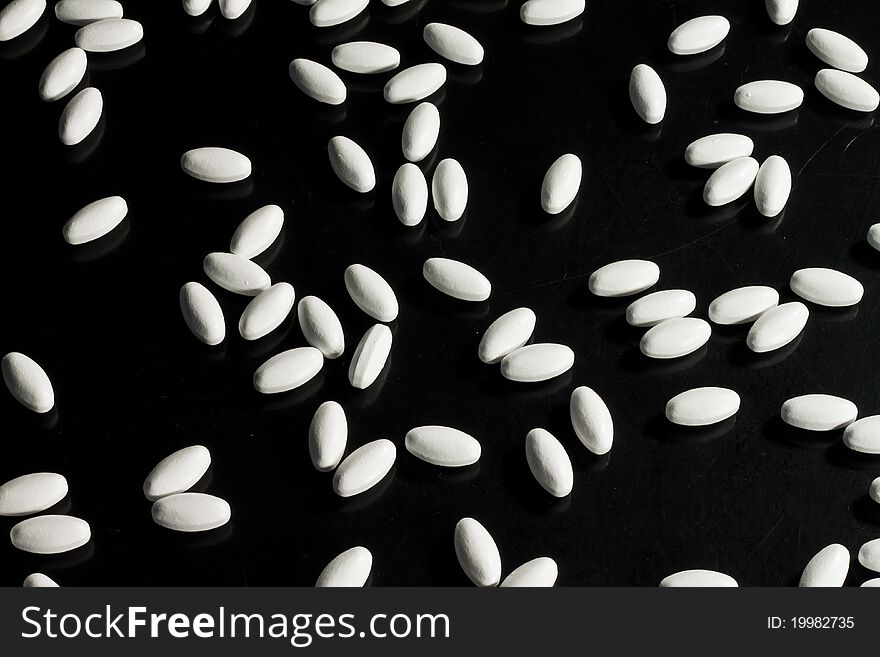 White pills spread out on black surface. White pills spread out on black surface
