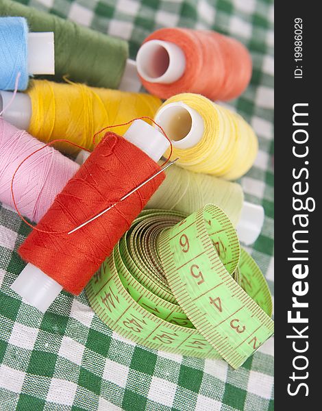 Coils with colored threads, needle on a checkered tablecloth. Coils with colored threads, needle on a checkered tablecloth