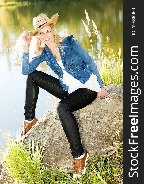 Young woman sitting on stone at pond