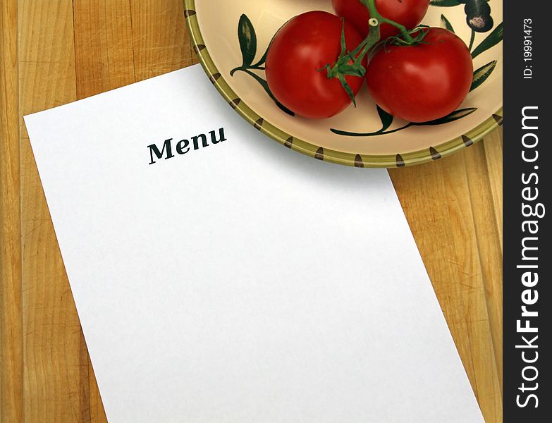 The word Menu on white paper with copy space, on cutting board with decorative bowl filled with tomatoes.