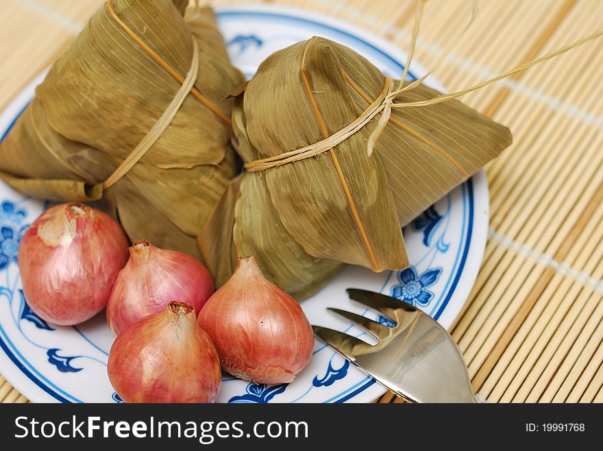 Traditionally wrapped rice dumplings and onions on plate. Traditionally wrapped rice dumplings and onions on plate.