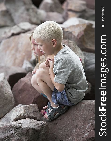 Little Boy And Girl Squat On Sharp Rocks