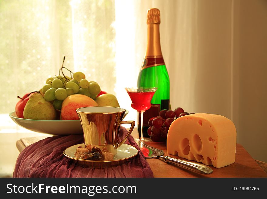 Grapes,apple,pear,cheese , glass with red wine,bottle and coffee in glold cup, on blurred background. Grapes,apple,pear,cheese , glass with red wine,bottle and coffee in glold cup, on blurred background.