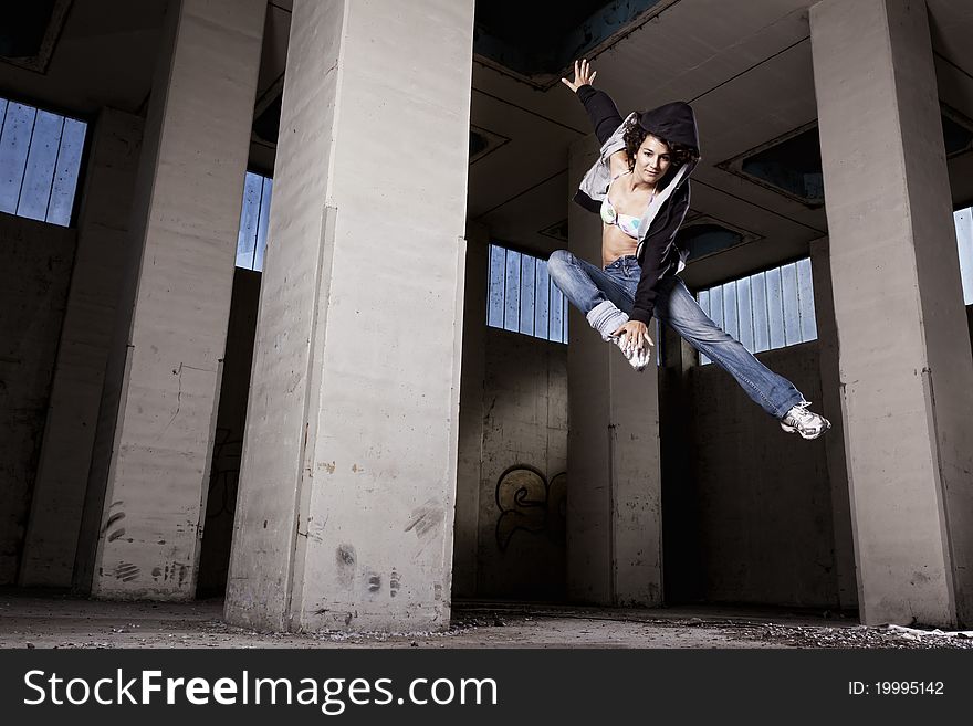 Modern hip hop dancer girl jumping high with one leg up in old dirty factory hall. Modern hip hop dancer girl jumping high with one leg up in old dirty factory hall.