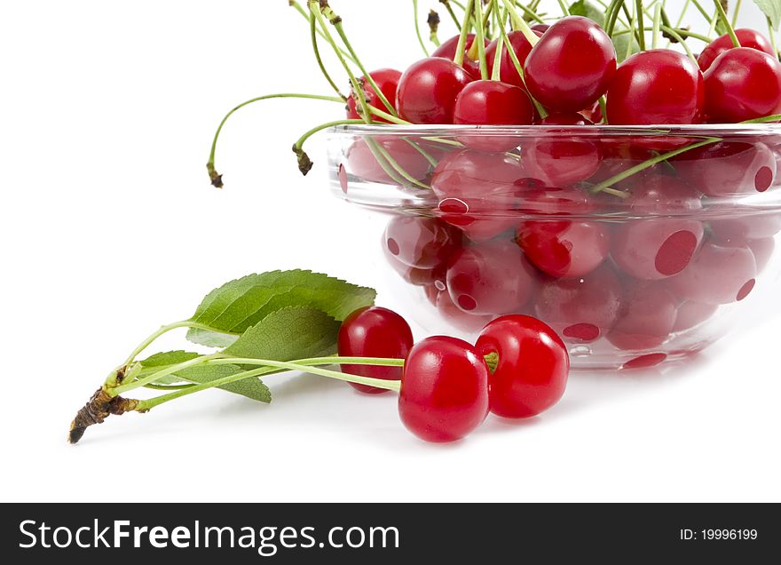 A cherry with a branch lies near a dish with a cherry