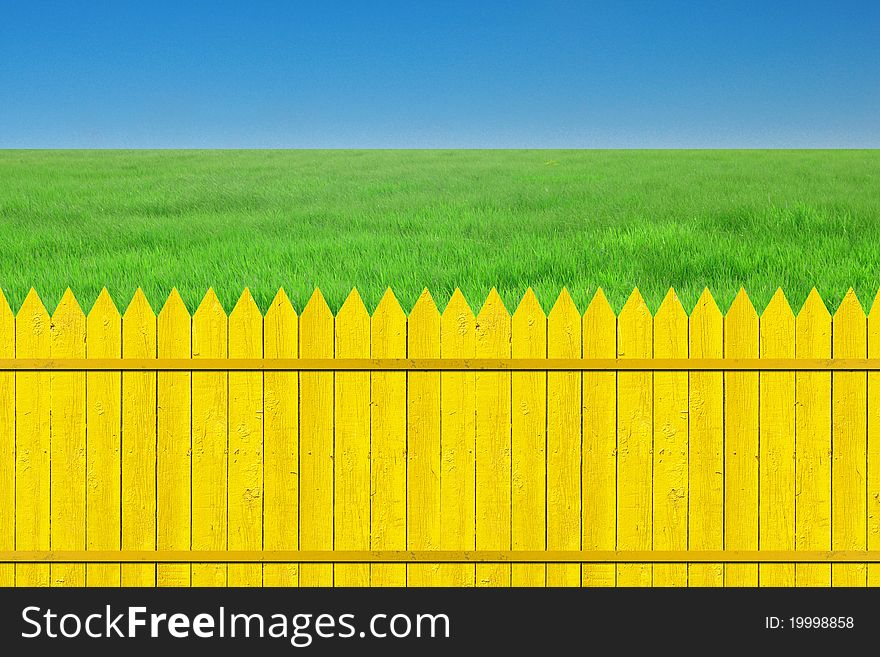 Yellow fence with grass on clear blue sky