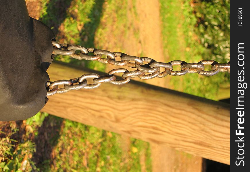 A rubber swing seat hanging on chains on a wooden frame. A rubber swing seat hanging on chains on a wooden frame.