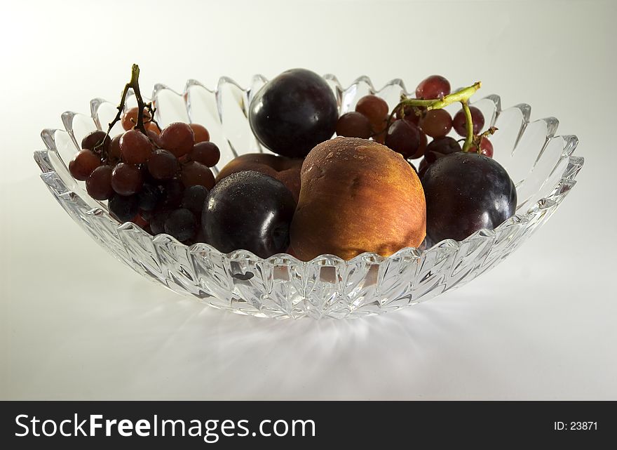 A crystal bowl filled with fruit, including peaches plums and grapes. A crystal bowl filled with fruit, including peaches plums and grapes