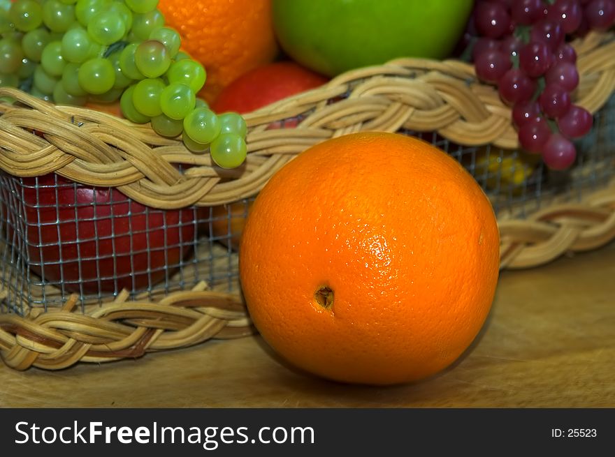 Photo of an Orange With Fruit Basket in Background.