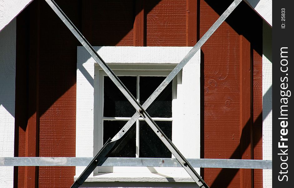 Window of farm milkhouse framed by windmill legs forming geometric designs. Window of farm milkhouse framed by windmill legs forming geometric designs.