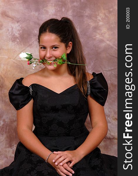 This is an image of a young girl, posing in a portrait, with a white rose in her teeth. This is an image of a young girl, posing in a portrait, with a white rose in her teeth.
