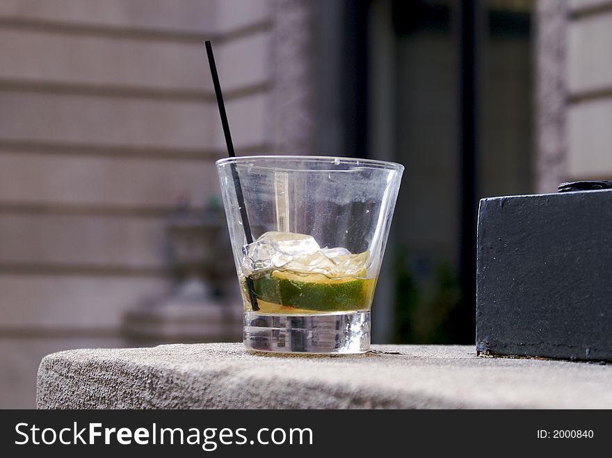 Outdoor gin and tonic, after the party a single glass sits on cement wall with nothing left but lime and ice with a straw. Outdoor gin and tonic, after the party a single glass sits on cement wall with nothing left but lime and ice with a straw