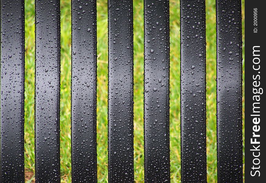 Black bench slats with rain drops, grass in background. Black bench slats with rain drops, grass in background
