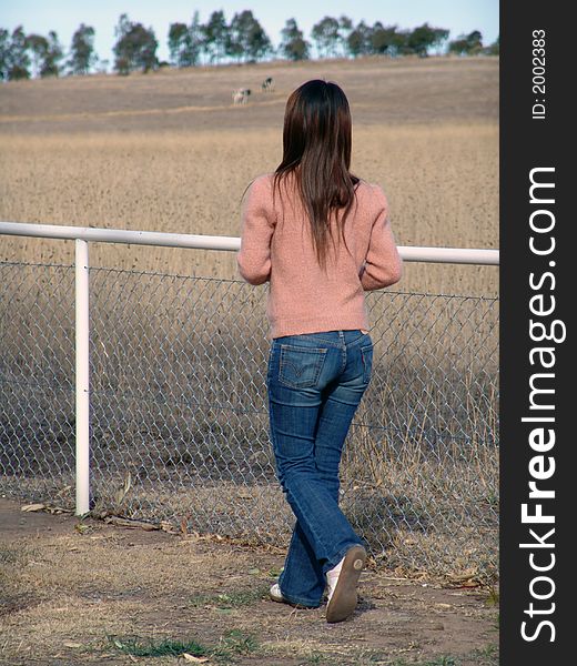 Girl enjoying the view of the land behind the fence. Girl enjoying the view of the land behind the fence