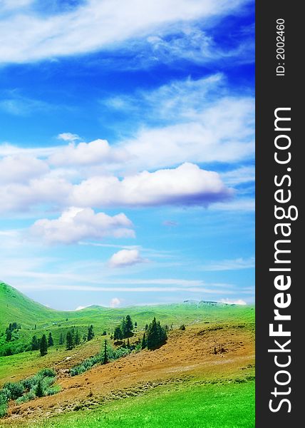 A green meadow in mountain with tree under the beautiful blue sky with clouds. A green meadow in mountain with tree under the beautiful blue sky with clouds