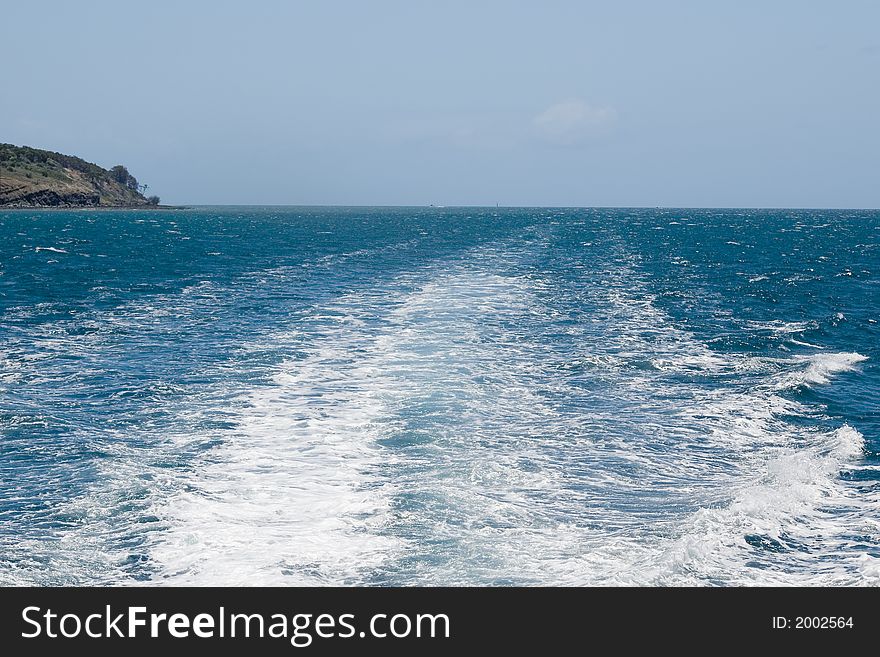 Looking out the back at a catamarans wake as it travels past an island. Looking out the back at a catamarans wake as it travels past an island