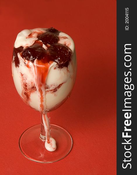 The glass with ice-cream with flow down strawberry jam over red background