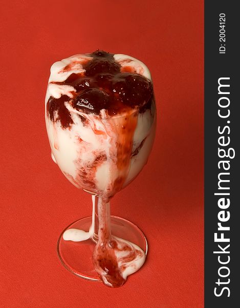 The glass with ice-cream with flow down strawberry jam over red background