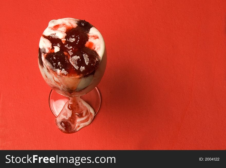 The glass with ice-cream with flow down strawberry jam over red background