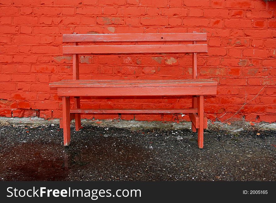 Old red bench by a red cracked brick wall. Old red bench by a red cracked brick wall
