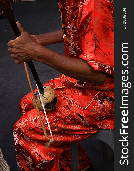 An old man wearing in red playing a Chinese instrument, er wu. An old man wearing in red playing a Chinese instrument, er wu.