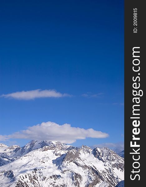 Snowed peak of a mountain surrounded by small cloud, a lot of blue for copy-space. Snowed peak of a mountain surrounded by small cloud, a lot of blue for copy-space