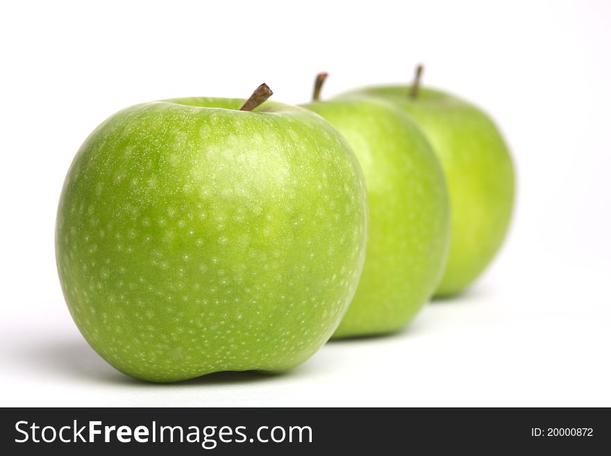 A row of green apples with stalks. A row of green apples with stalks