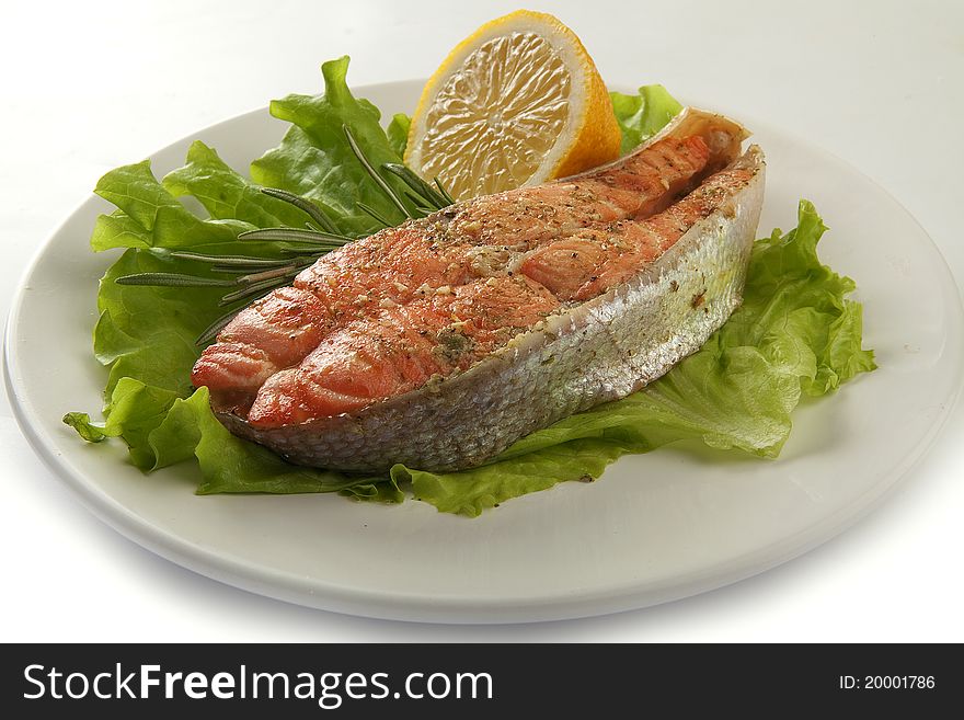 Fried trout with lettuce, lemon and rosemary on the plate. Fried trout with lettuce, lemon and rosemary on the plate