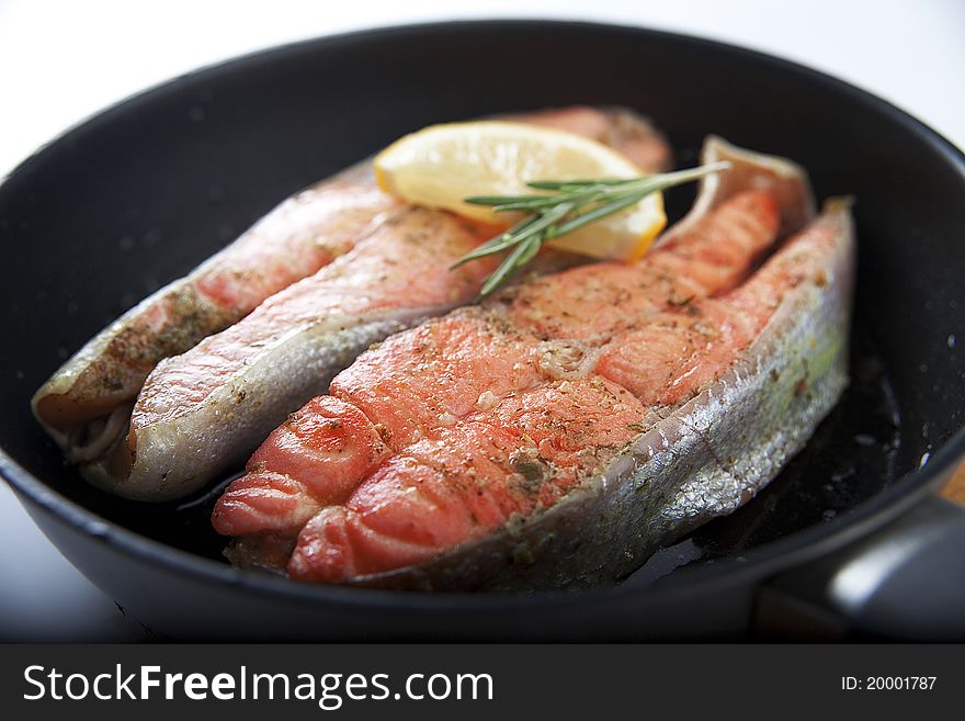 Fried trout with lemon and rosemary on the black pan. Fried trout with lemon and rosemary on the black pan