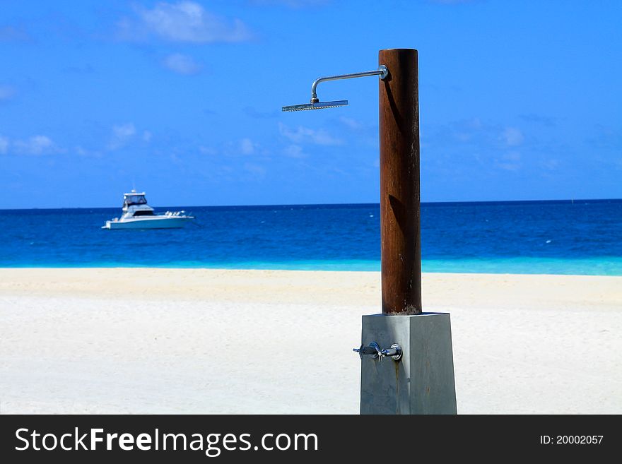 A shower head stands on a white pristine sandy beach against the backdrop of a blue/turquoise tropical sea. A shower head stands on a white pristine sandy beach against the backdrop of a blue/turquoise tropical sea