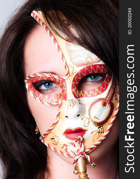 Beautiful young brunette haired, blue eyed model dressed in gold with colorful red and gold venetian carnival face mask. Beautiful young brunette haired, blue eyed model dressed in gold with colorful red and gold venetian carnival face mask