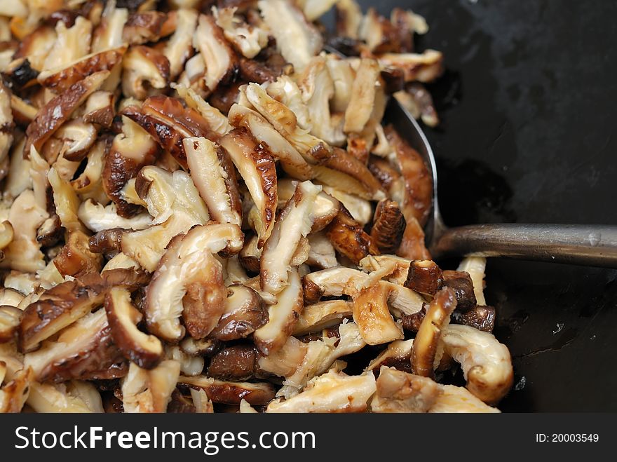 Cooking fragrant mushroom slices in traditional Chinese wok. Cooking fragrant mushroom slices in traditional Chinese wok.