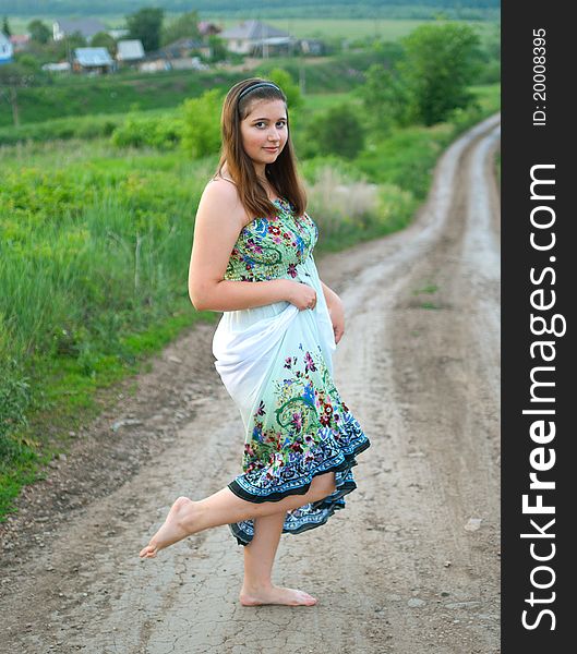The portrait of young smiling girl in light dress on the road