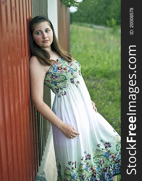 Young beautiful girl in light dress against metal fence