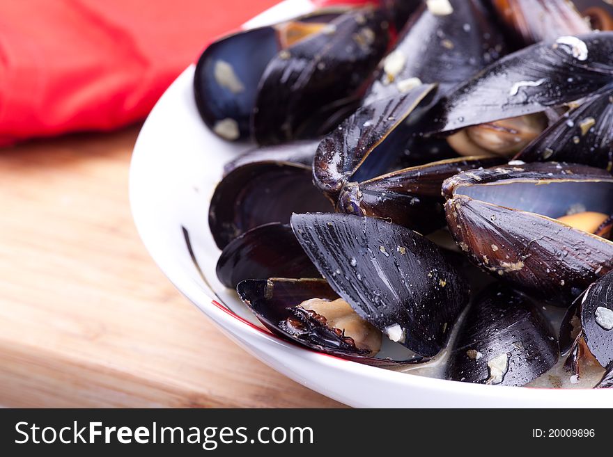 Close up picture of mussels in the bowl on wooden board.