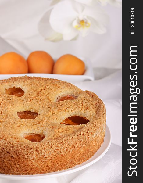 Apricot tart on a cake stand with apricots and flowers out of focus in the background