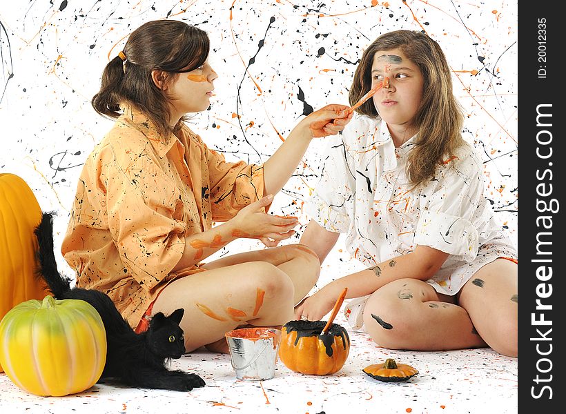 Two sisters painting each other and making a mess with Halloween colored paint. Pumpkins and a black cat are nearby. Two sisters painting each other and making a mess with Halloween colored paint. Pumpkins and a black cat are nearby.