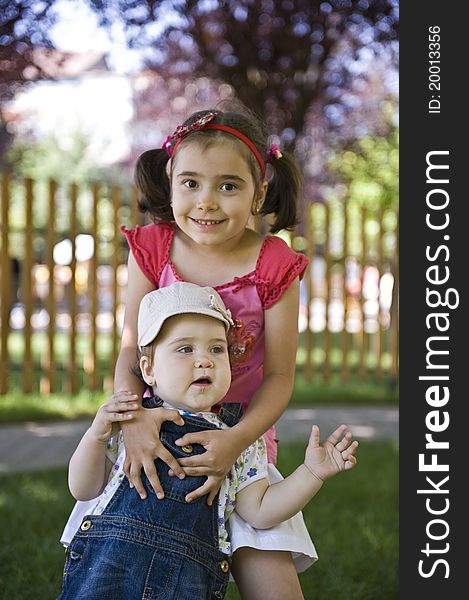 Two sisters sitting outdoors smiling and hugging. Two sisters sitting outdoors smiling and hugging