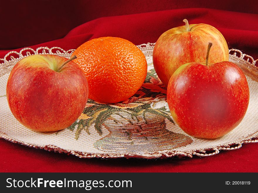 Three apples and one orange on serviette. Red studio background