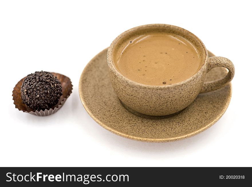 A cup with coffee standing on a saucer and a candy beside them on the white background. A cup with coffee standing on a saucer and a candy beside them on the white background