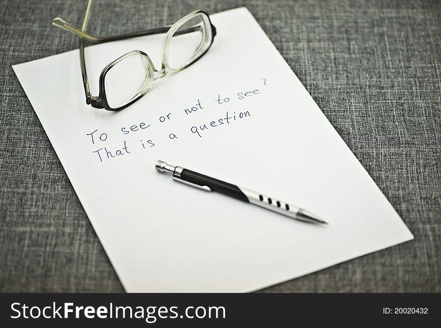 A Sheet of Paper and a Pen and Glasses on It on the Grey Background