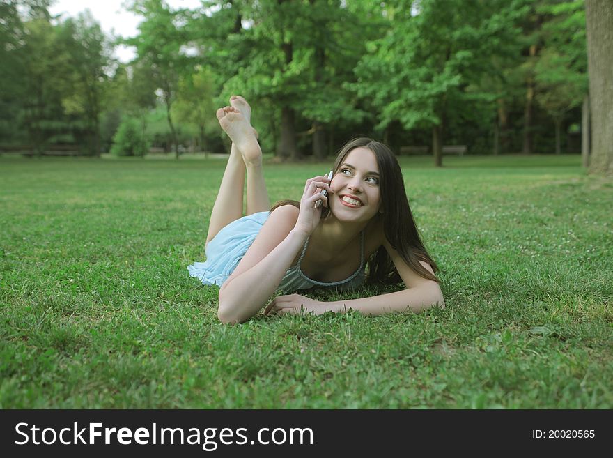 Smiling woman lying on a green meadow and talking on the mobile phone. Smiling woman lying on a green meadow and talking on the mobile phone