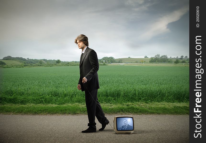 Young businessman walking on a countryside road and carrying a television. Young businessman walking on a countryside road and carrying a television