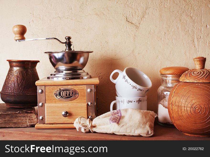 Coffee still life (grinder, cup, a turk, a bag of beans, a jar) against the background of an old wall